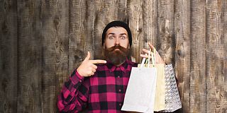 Junger Mann mit Bart zeigt auf Einkaufstüten