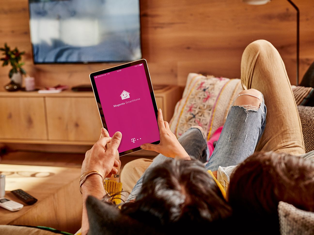 Zwei Personen liegen gemütlich auf dem Sofa und steuern bequem per App die Geräte im Wohnzimmer.
