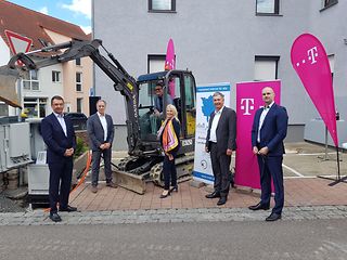 Vertreter der Gigabitregion Stuttgart und der Telekom Region Südwest stehen vor einem Bagger.