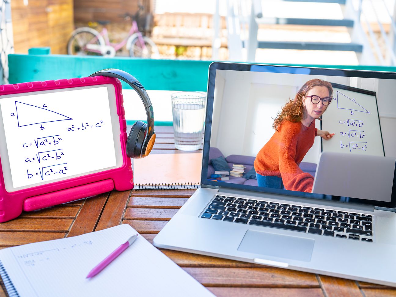 Auf dem Tisch steht ein Laptop mit laufender Homeschooling-Session und daneben Tablet und Schreibblock.