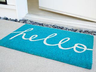  Eine geöffnete Haustür und eine Fußmatte mit dem Schriftzug „Hello“.