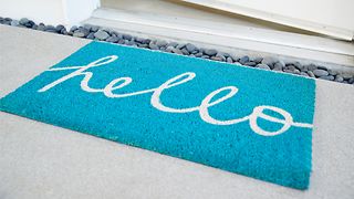 An open front door and a doormat with the writing "Hello".