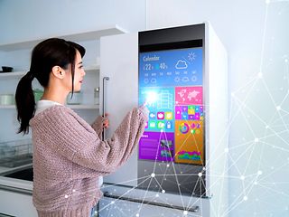  A woman in front of a refrigerator with a monitor on the door.