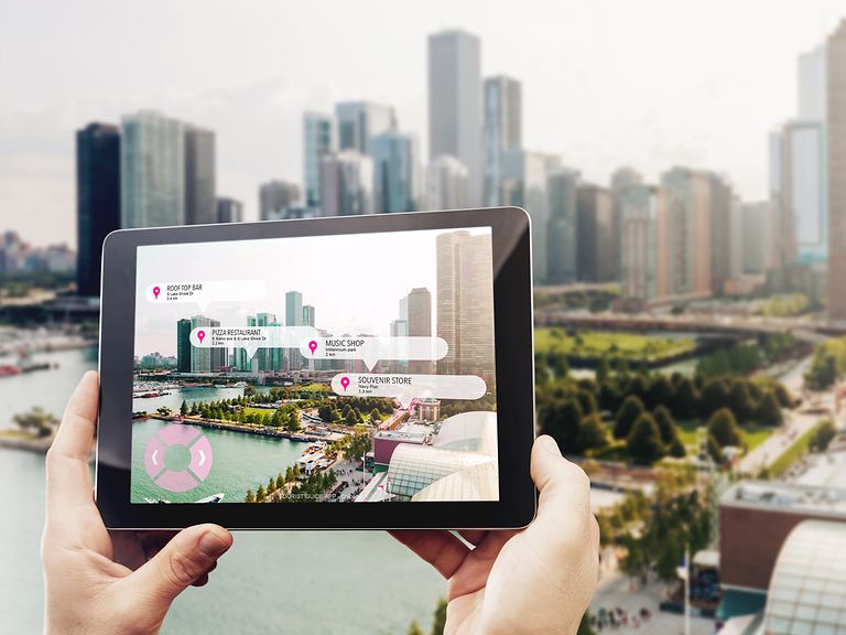 Hands holding a tablet showing relevant places in the city which are in front of the tablet.