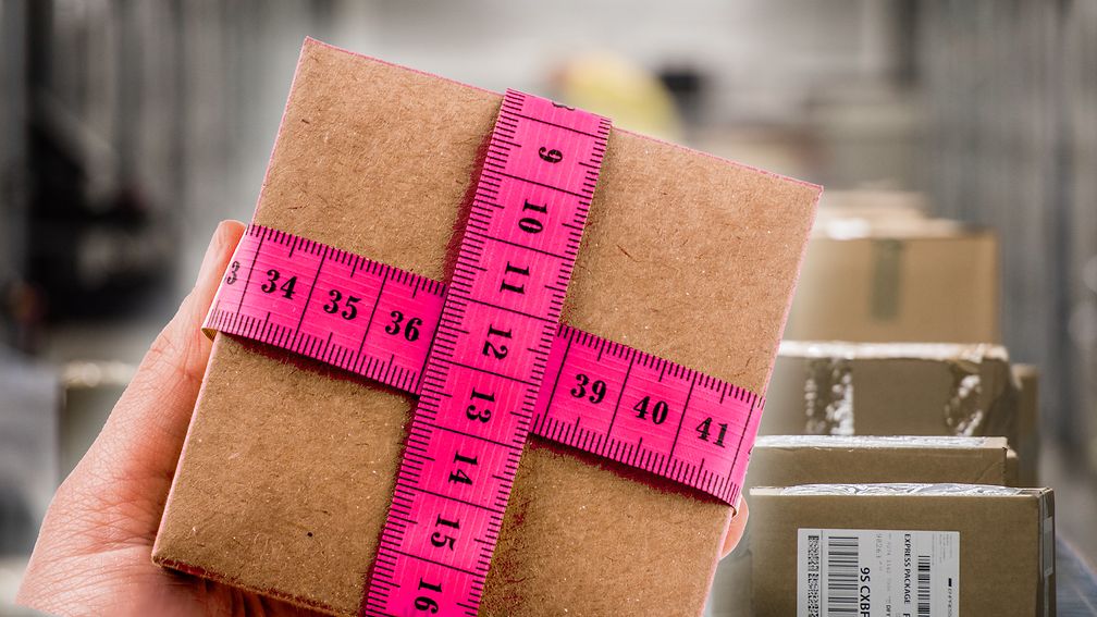 Eine Hand hält ein kleines Paket, das mit magentafarbenen Maßband umwickelt ist.