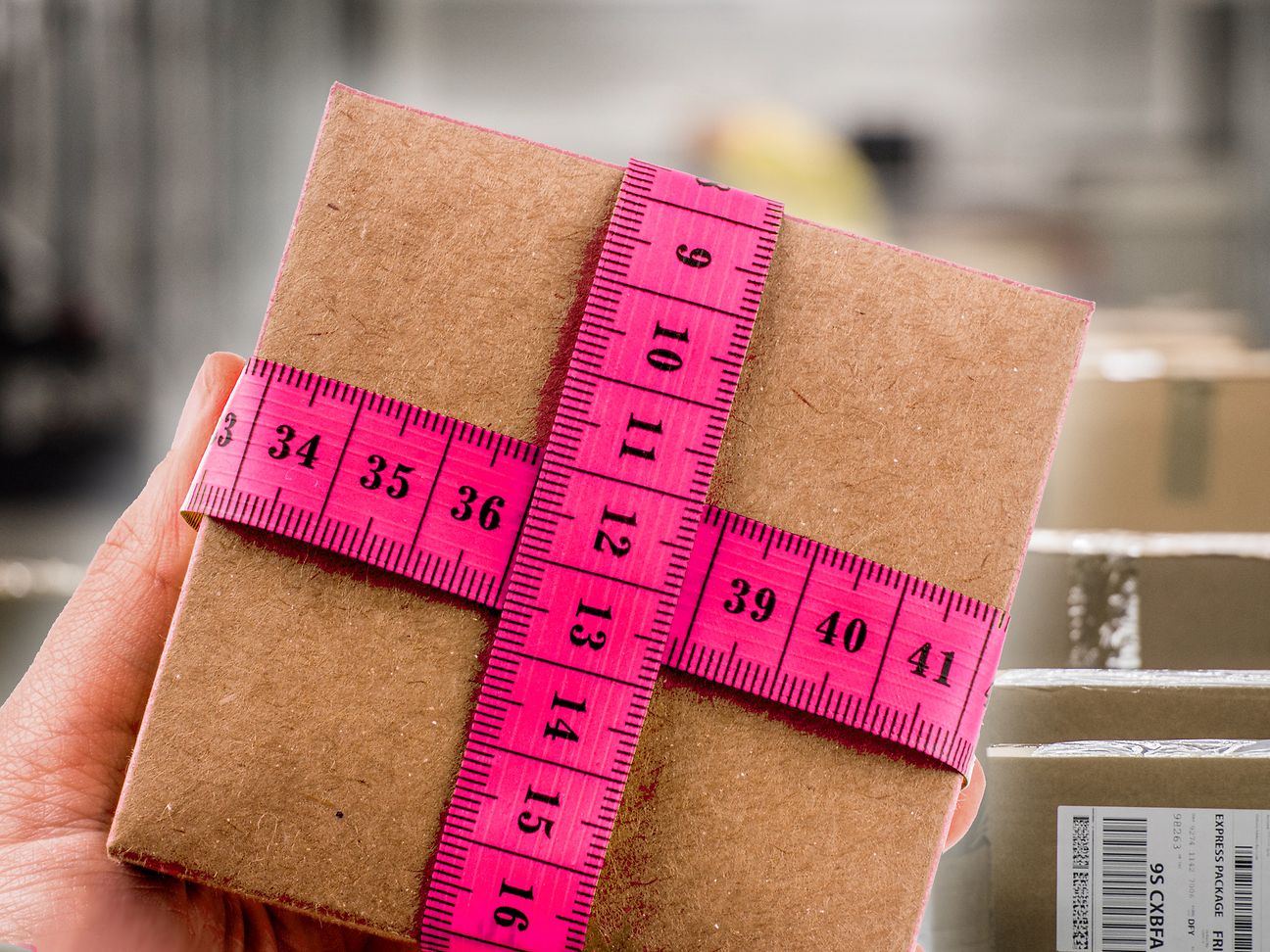 Eine Hand hält ein kleines Paket, das mit magentafarbenen Maßband umwickelt ist.