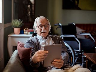  Ein Rentner mit Kopfhörer und Tablet auf dem Sofa.