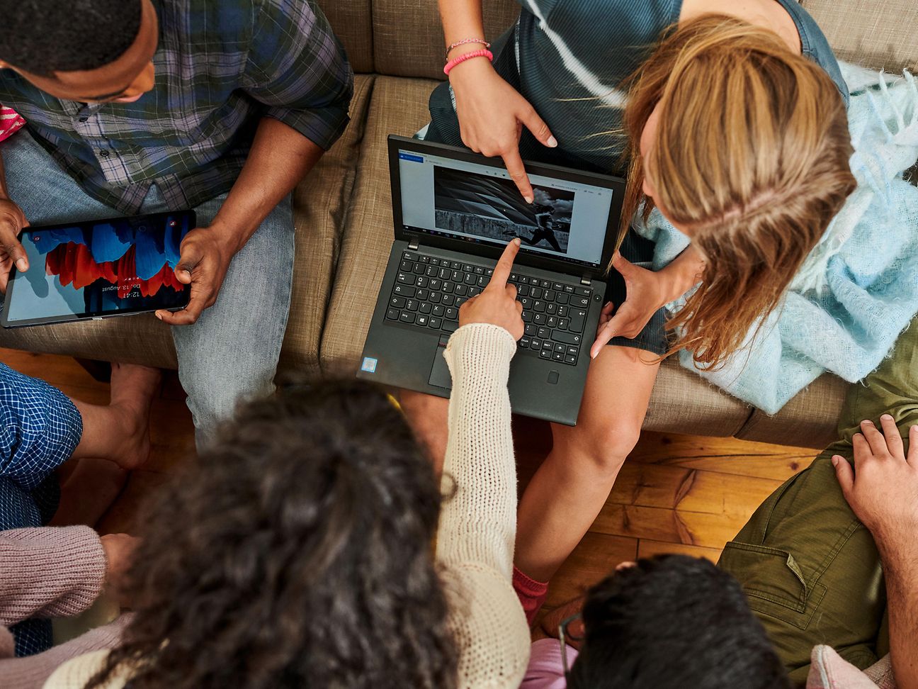 Gruppe von Menschen sitzen um einen Laptop und zeigen mit dem Finger auf den Bildschirm.