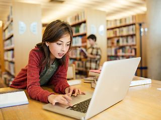 Mädchen in Bibliothek an einem Notebook