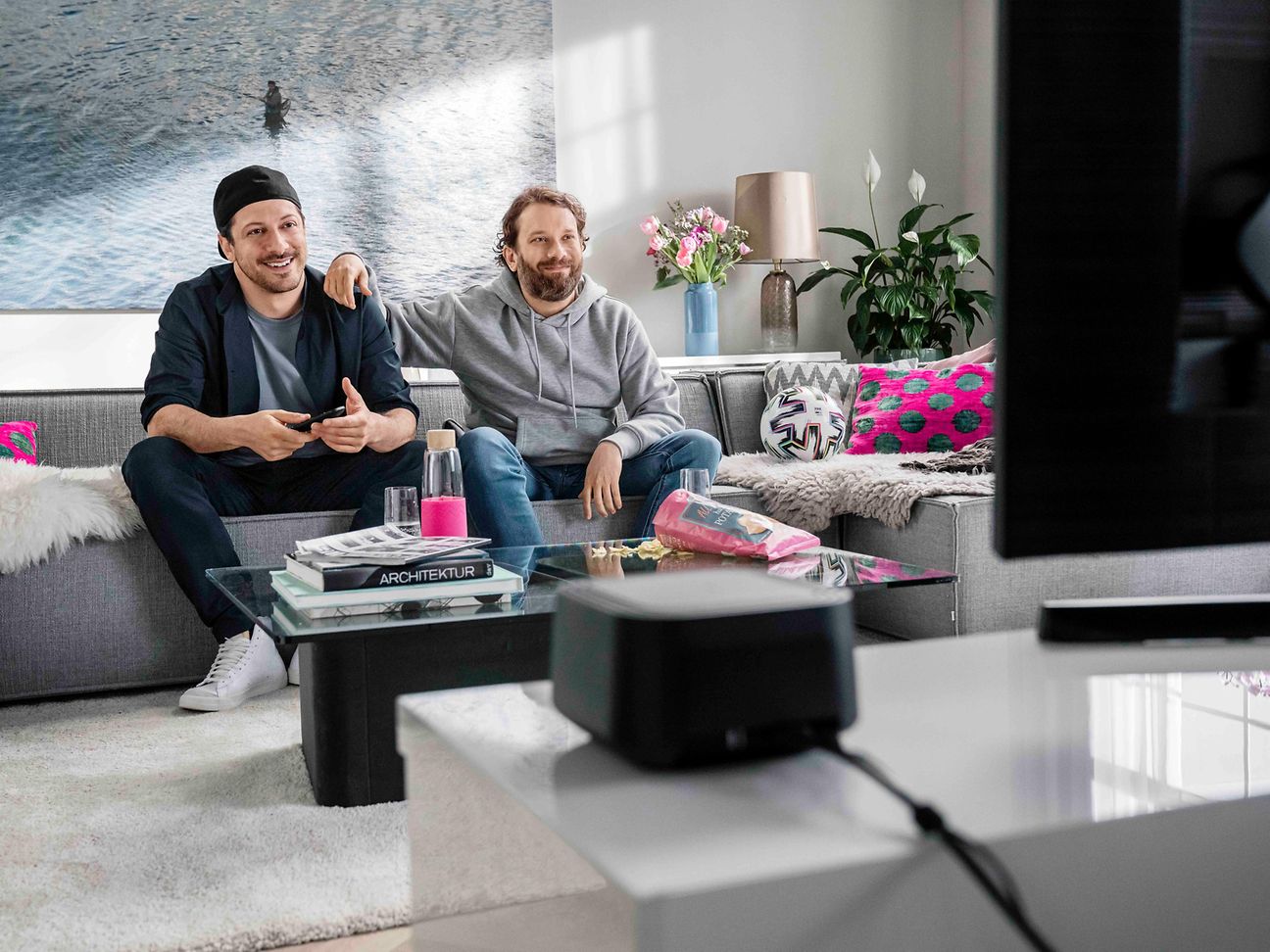 Fahri Yardim (l.) und Christian Ulmen vor einem Fernseher.