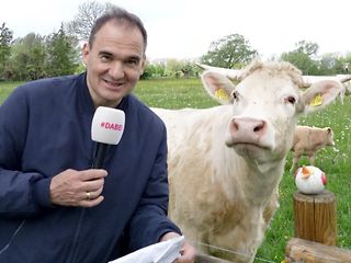 Ein Pressesprecher der Telekom steht mit einem Mikrofon neben einer Kuh.