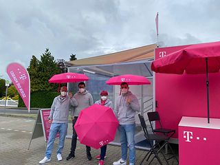 Vier Telekom Beschäftigte stehen mit magenta Regenschirmen vor dem Servicemobil