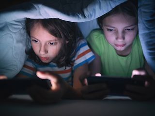 Kinder unter der Bettdecke schauen auf Smartphones
