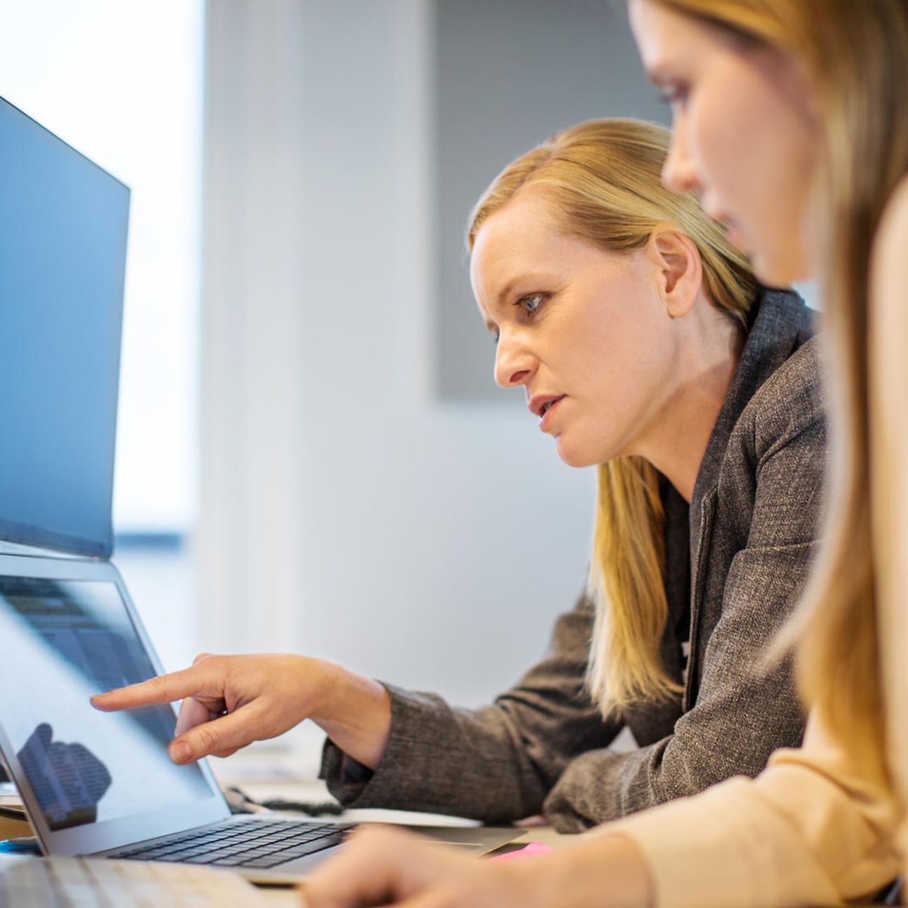 Eine Frau erklärt einer anderen etwas an einem Laptop in einem Büro