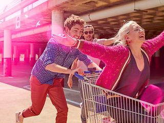 Young man pushes a shopping trolley in which a young woman is sitting.