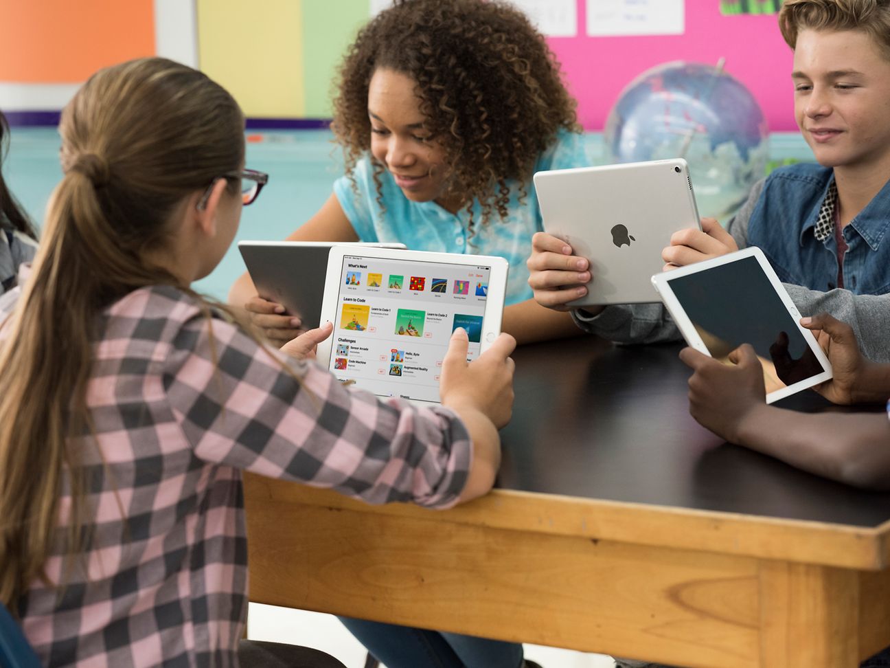 Schüler*innen sitzen am Tisch und haben iPads in der Hand