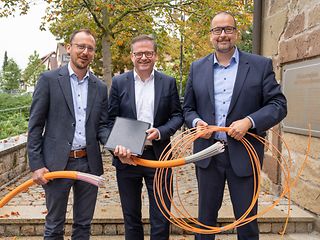 Die drei Genannten halten die Vertragsmappe und Speedpipe-Stücke in den Händen. 