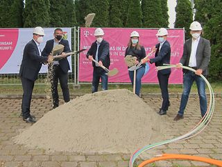 Die in der Bildunterschrift genannten Personen stehen mit Abstand nebeneinander vor einem Sandberg an der Baustelle.