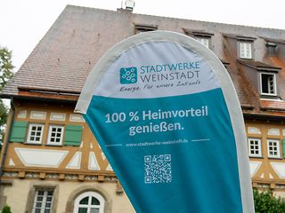 Eine Beachflag der Stadtwerke Weinstadt steht vor dem Fachwerk-Gemeindehaus. 