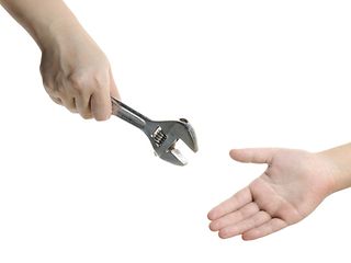 Eine Hand reicht einen Schraubenschlüssel in eine andere Hand