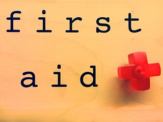 Schriftzug first aid mit roten Kreuz als Pin