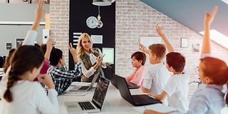 Schüler*innen sitzen mit Lehrerin am Tisch mit Laptops vor sich.