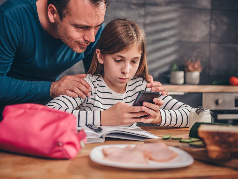 Vater mit Tochter am Tisch. Beide schauen auf ein Handy.