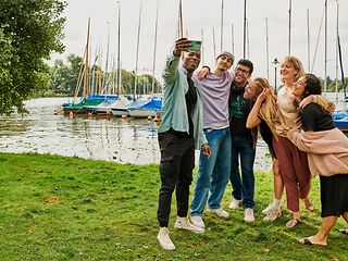 A group of young people taking a selfie against a rural backdrop by the lake.