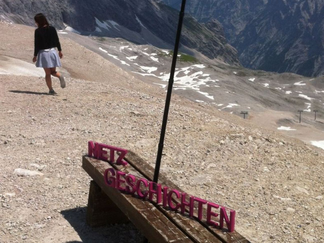 Netzgeschichten Ein Aufsteller der Netzgeschichten steht auf einer Bank vor einem Bergpanorama