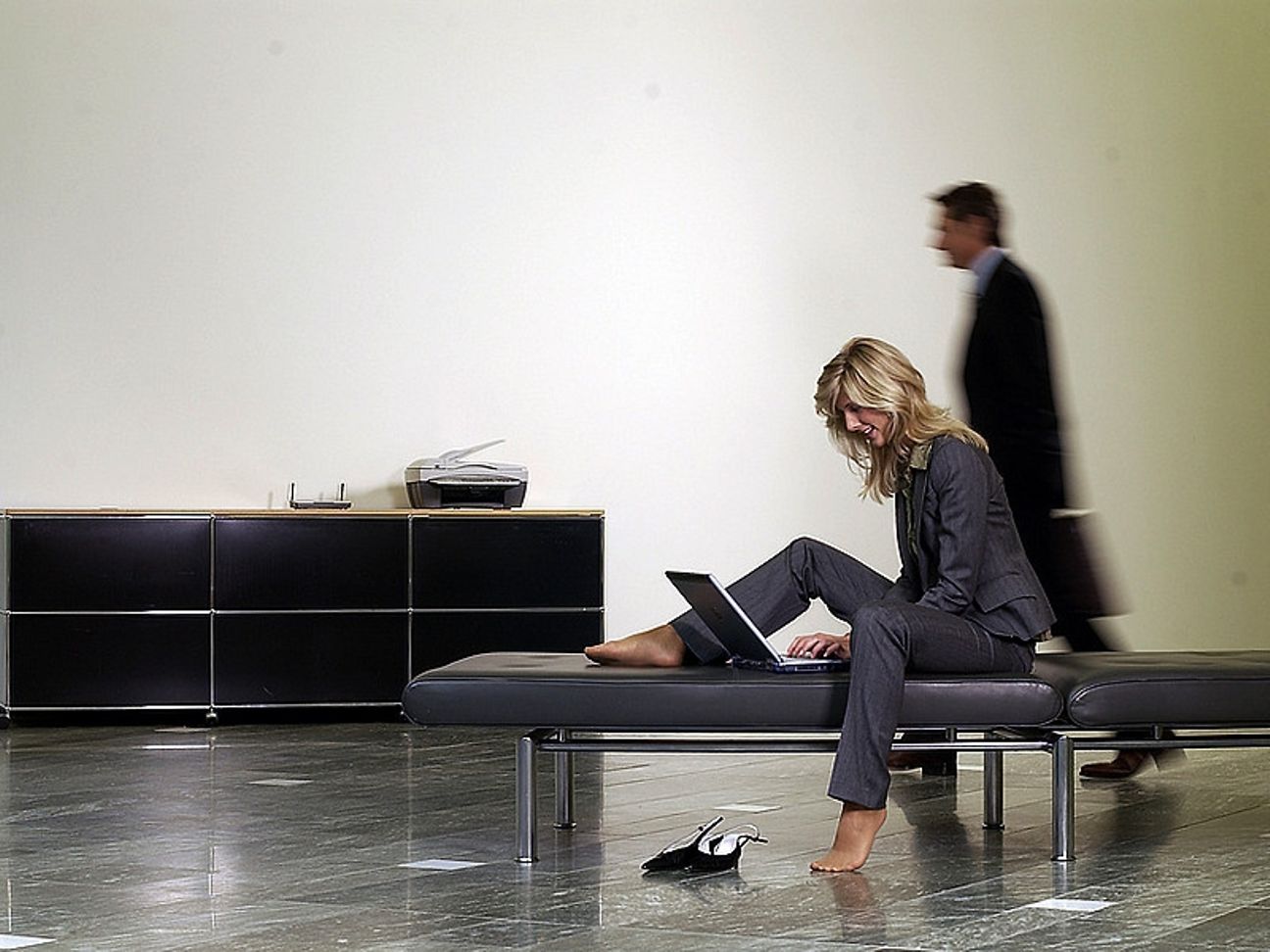 Eine Frau sitzt ohne Schuhe auf einer Bank in einem Büro.