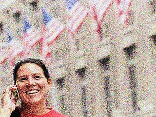 Eine lächelnde Frau telefoniert vor mehreren USA-Flaggen.