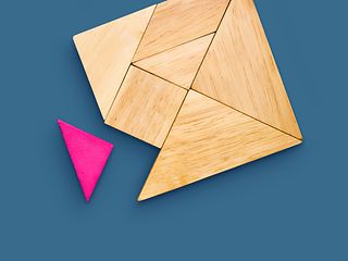 A wooden tangram lies on a blue background. One of the parts is not inserted and is colored magenta. 