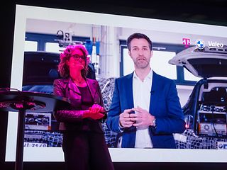 Claudia Nemat auf der Bühne des Telekom-Standes. Dahinter Nicolai Martin, SVP BMW Group Driving Experience, im Video.