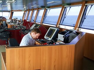 Ein Mann arbeitet am PC an Bord eines Schiffes.