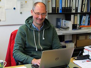 Rolf Schmidt sitzt an seinem Schreibtisch.
