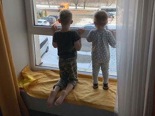 Yaroslava's children Misha (6) and Marko (1) stand together at the window and look out onto the street.