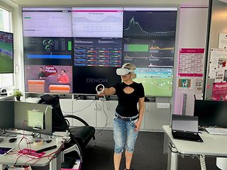 Frau steht mit einer VR-Brille vor großen Monitoren